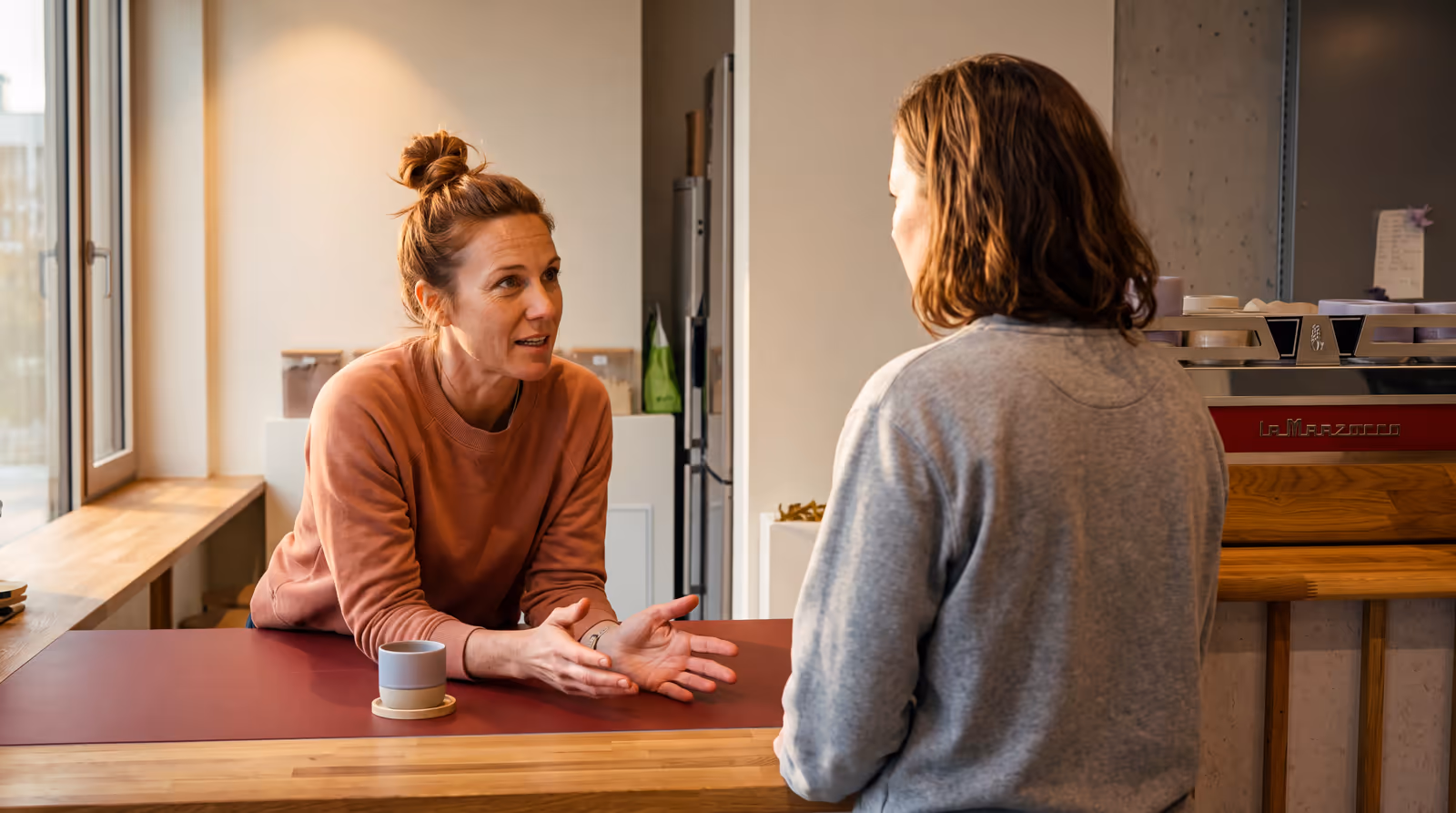 Zwei Frauen im Gespräch an der Theke im Studio, eine erklärt mit offenen Händen
